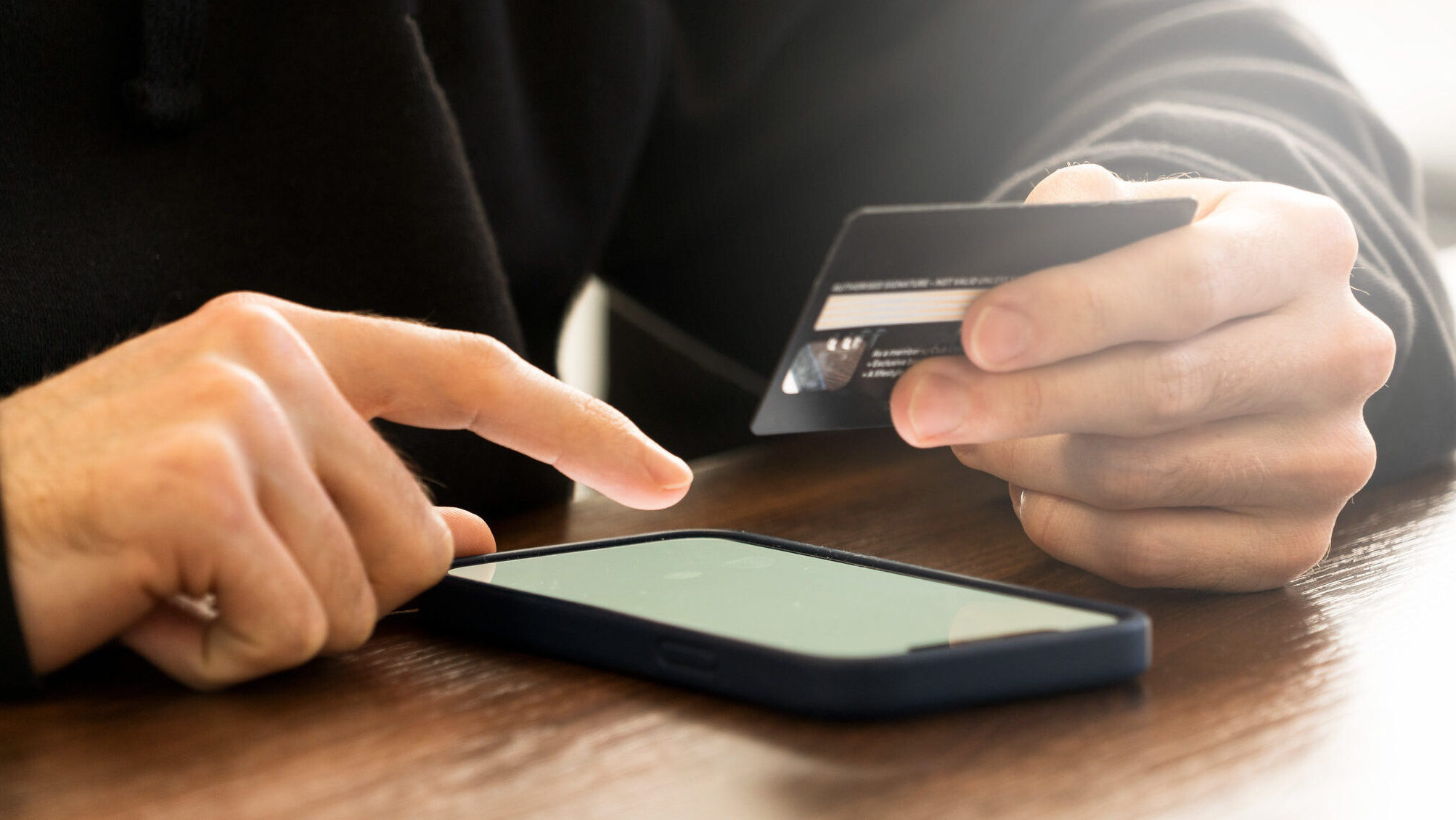 Osoba unosi podatke sa kartice u mobilni telefon radi plaćanja robe preko interneta